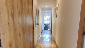 A hallway with a polished stone floor, wooden doors, and framed pictures on the walls. - Bright 3BR Oasis • 500Mbps WiFi & 24/7 Security (Medellín)
