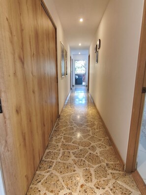 A hallway with a polished stone floor, wooden doors, and framed pictures on the walls. - Bright 3BR Oasis • 500Mbps WiFi & 24/7 Security (Medellín)