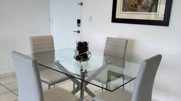 Un comedor moderno con una mesa de vidrio y cuatro sillas, un cuadro enmarcado en la pared y una puerta con manija.