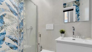Ein modernes Badezimmer mit Duschkabine aus Glas, Toilette, Waschbecken mit Spiegel darüber und einer kleinen Topfpflanze auf dem Waschbecken.