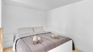 Ein schlicht eingerichtetes Schlafzimmer mit einem Bett, Kissen und ordentlich gerollten Handtüchern.