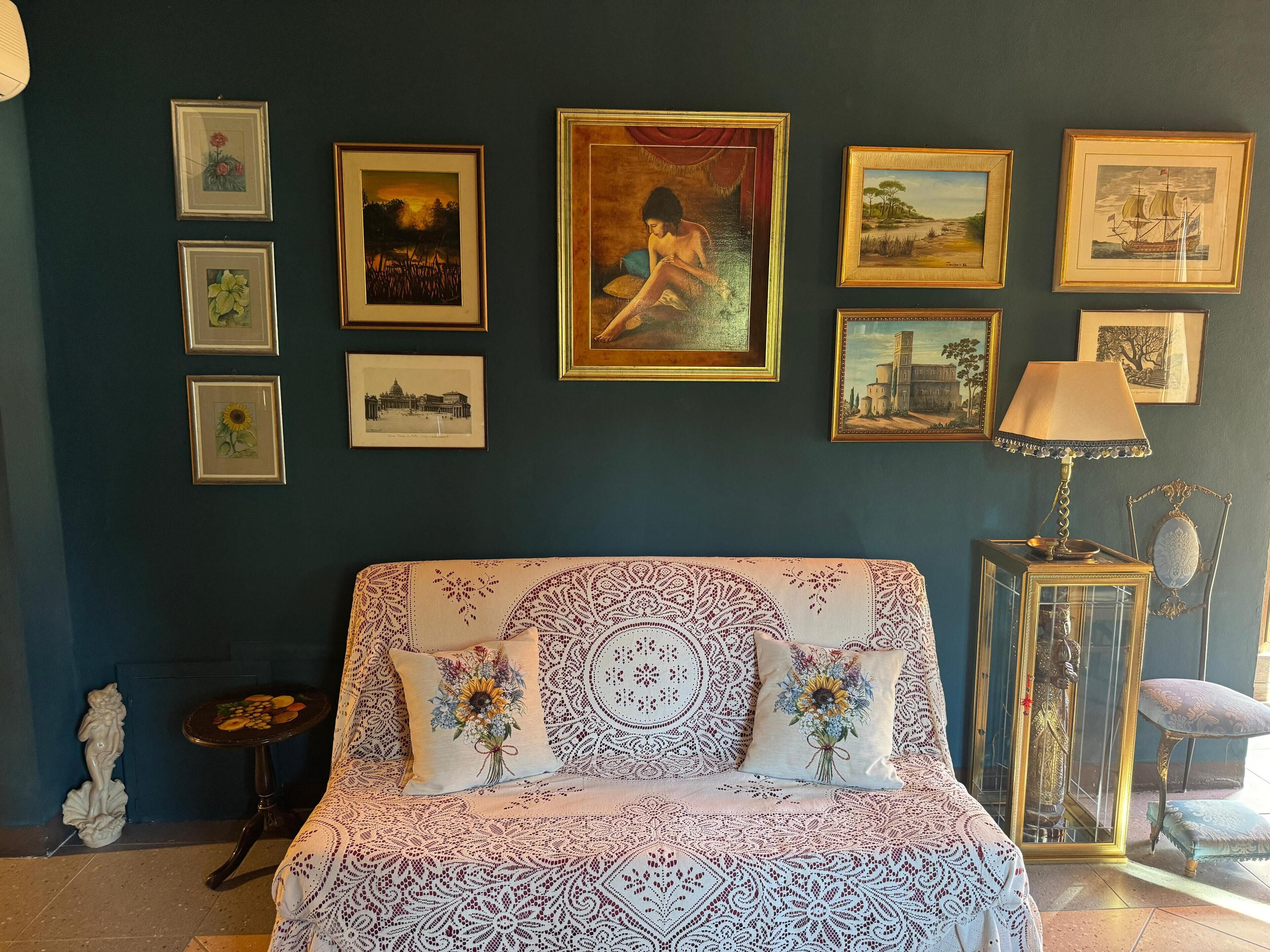 Una habitación con cama, una obra de arte en la pared, una lámpara y una mesita con adornos.