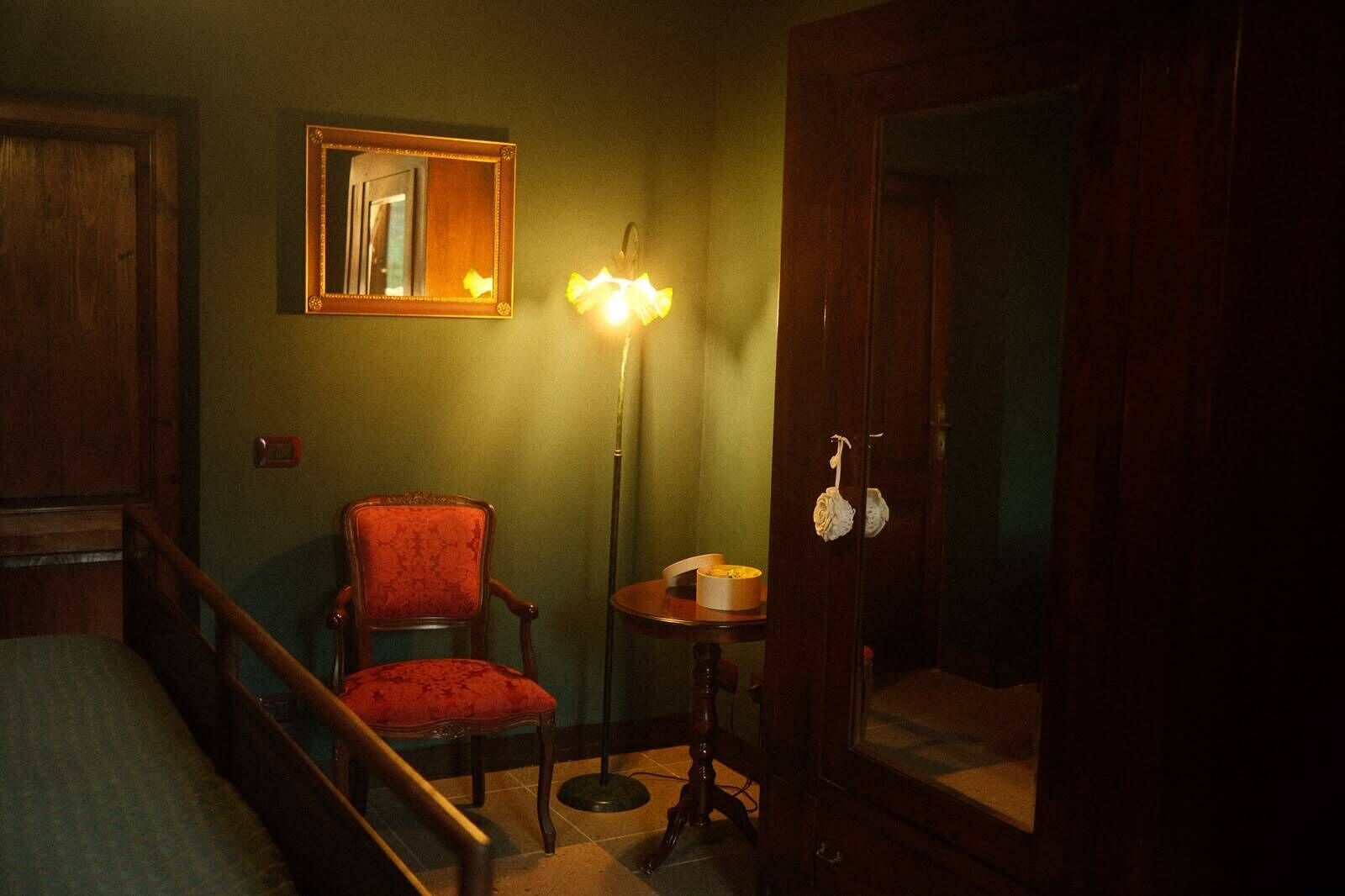 A room with a wooden chair, a floor lamp, a mirror, and a door.
