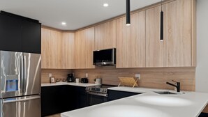A modern kitchen with a stainless steel refrigerator, a built-in oven, a microwave, and a wooden cabinet.