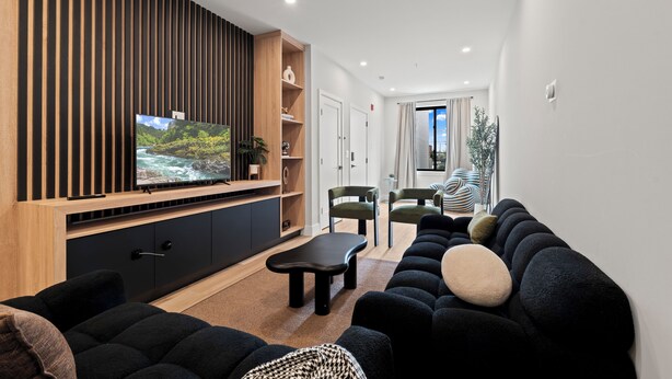 A modern living room with a flat-screen TV, dark sofas, a coffee table, and a wooden accent wall.