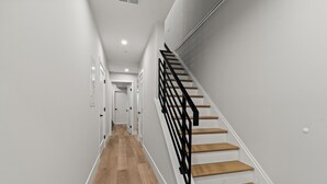 A modern staircase with wooden steps and black railings, leading to a hallway with white walls and wooden flooring.