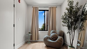A modern living room with a striped sofa, a potted plant, and a view through a window with curtains.