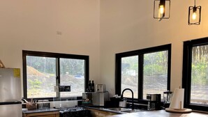 A kitchen with wooden cabinets, a stainless steel refrigerator, a stove, and a sink. There are two windows providing views of the outdoors. - Luxury cabin / Playa Venao (playa venao)
