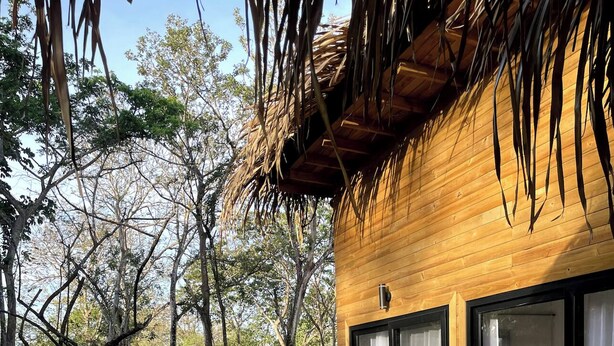 A wooden deck with wicker furniture, a glass door leading to a room, and a thatched roof structure. - Luxury cabin / Playa Venao (playa venao)