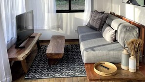 A modern living room with a sofa, TV, wooden coffee table, and a view of the outdoors through a window. - Luxury cabin / Playa Venao (playa venao)
