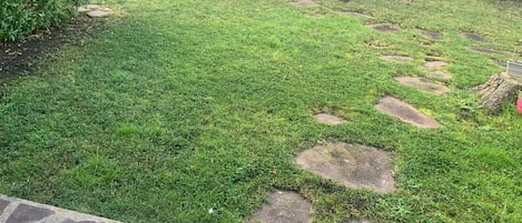 Un espacio al aire libre con césped, piedras para pisar y una silla de plástico blanca.