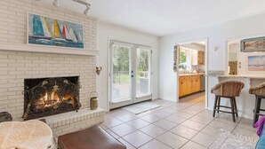 A living room with a fireplace, a painting, and a view into the kitchen. - The Silver Shell SSI - Dog Friendly (St. Simons Island)