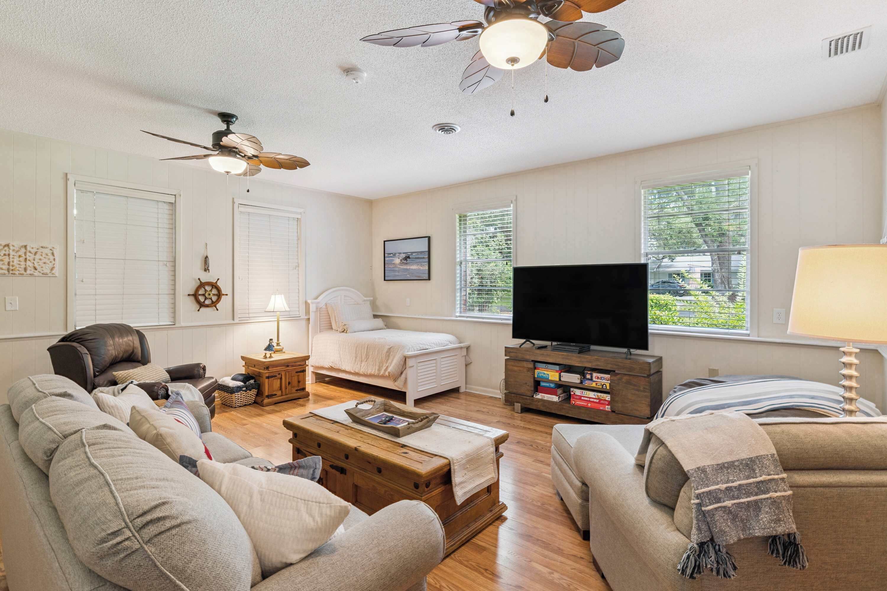 Una sala de estar con sofá, sillón, mesa de centro, televisor y ventilador de techo.