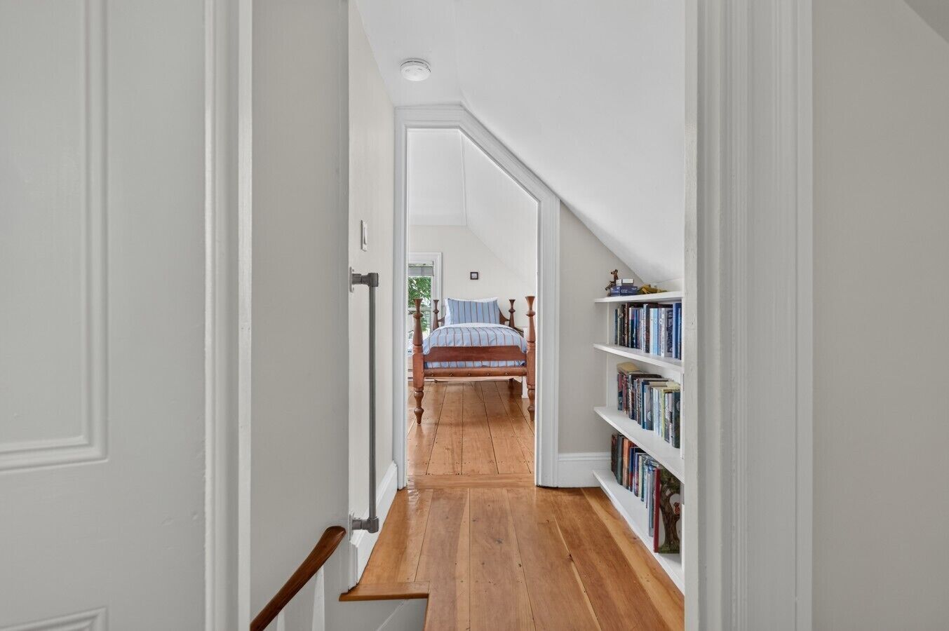 Un corridoio stretto che porta a una camera da letto con un letto e una libreria.