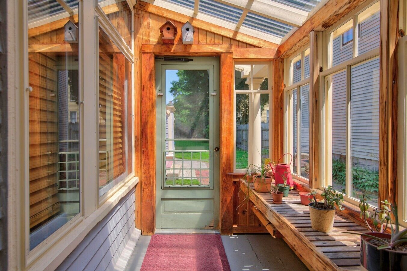 Een houten veranda met een groene deur, bloempotten en een rode gieter.