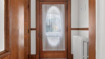 Una puerta de madera con una cortina blanca, un radiador y una pared blanca con adornos de madera.