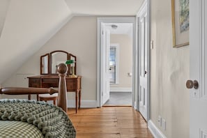 Ein Schlafzimmer mit einem Holzkapfenkasten, einem Stuhl, einem Bett mit grüner Decke und einer Tür zu einem weiteren Raum.