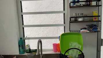 A kitchen with a stainless steel sink, a window with horizontal blinds, and shelves with various items including bottles and containers.