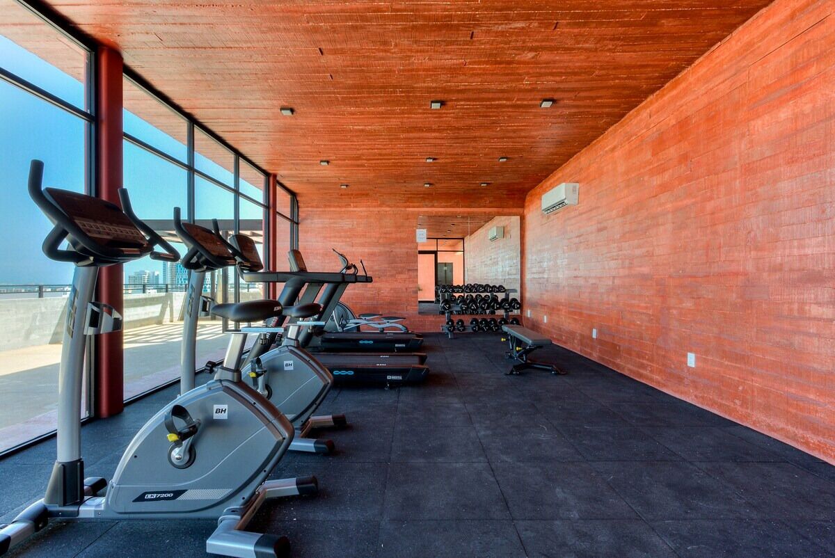 Un gimnasio con máquinas de cardio, pesas y un amplio ventanal.
