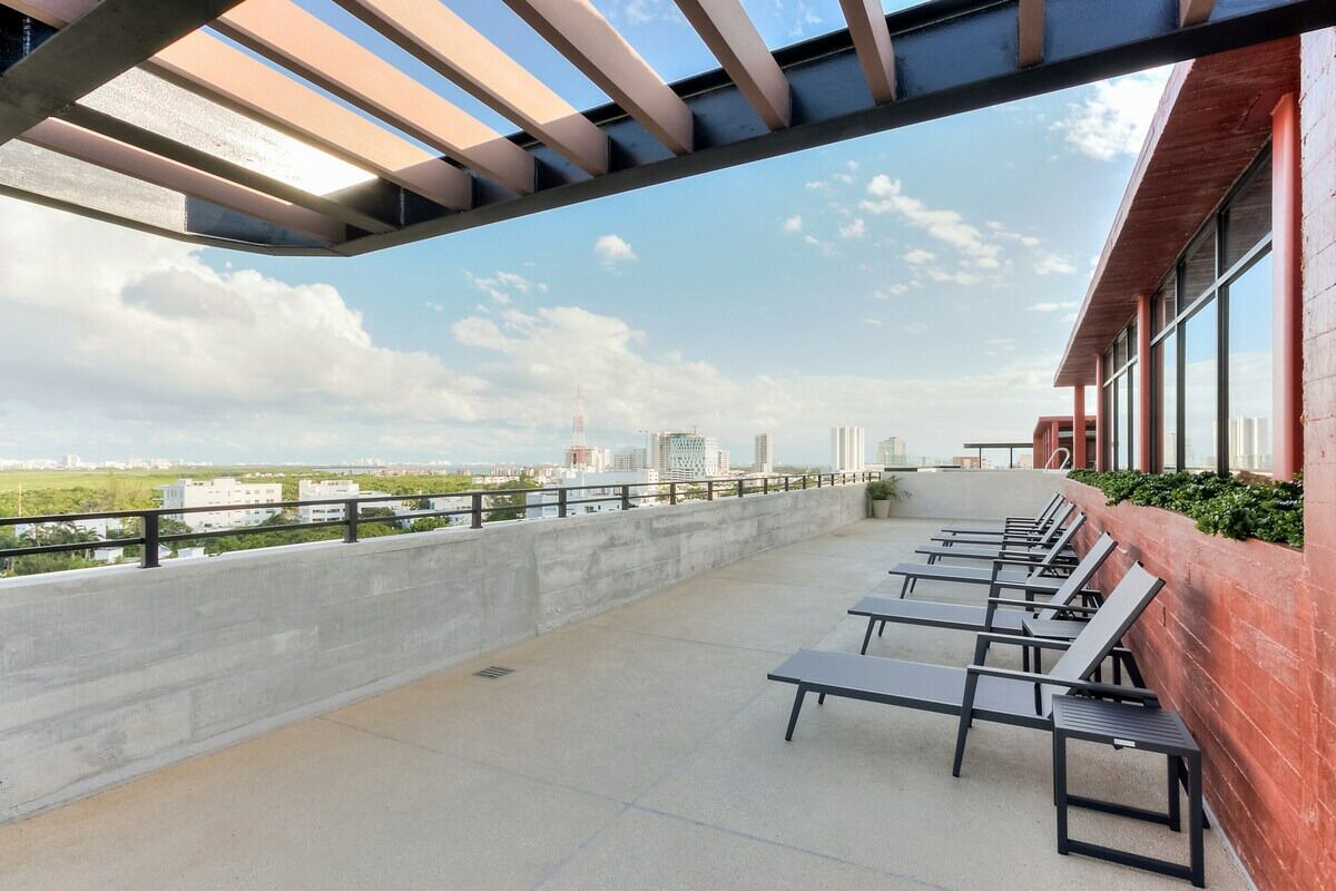 A rooftop terrace with sun loungers, a concrete floor, and a view of the city skyline.