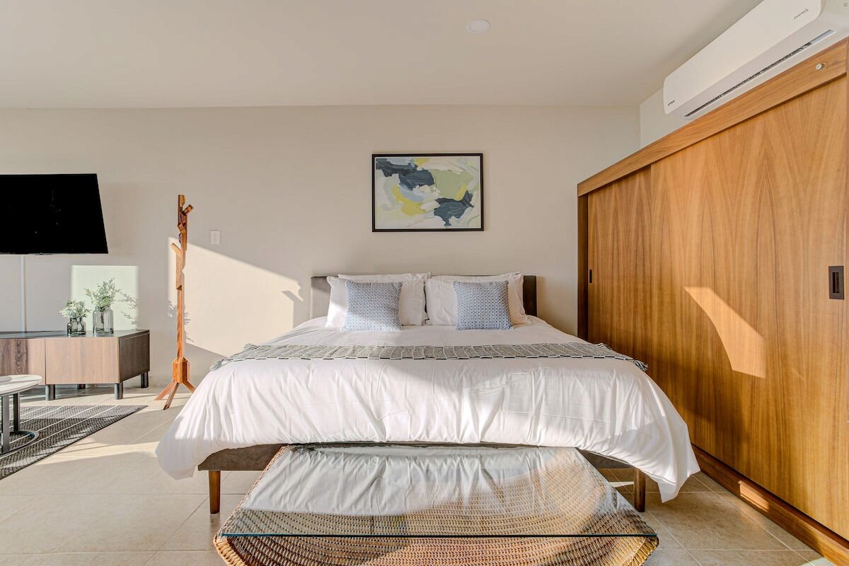 A modern bedroom with a large bed, a wooden wardrobe, a mounted TV, and a wall-mounted artwork.