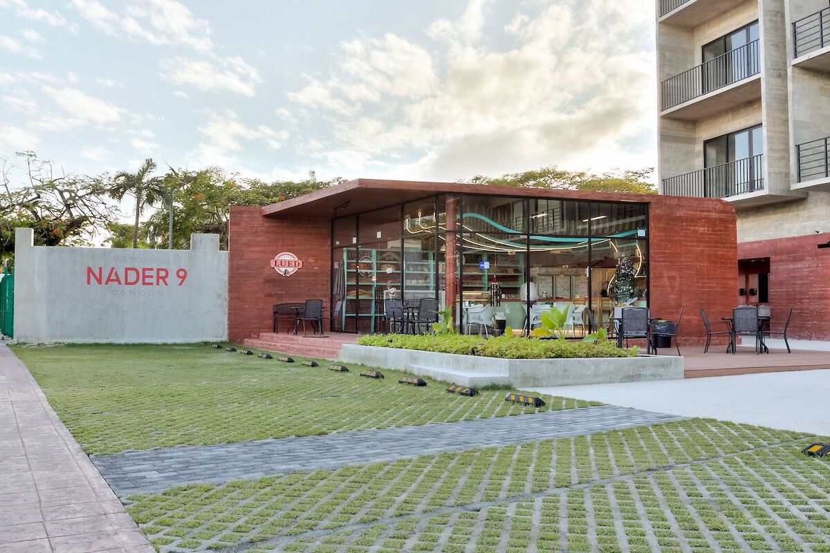 Een modern gebouw met een bord waarop 'NADER 9' staat en een overdekt terras met tafels en stoelen.