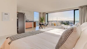 Una habitación de hotel moderna con una cama grande, un área de comedor y vistas a un paisaje urbano.