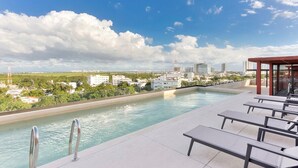 Una piscina en la azotea con sillones de descanso, vistas despejadas del horizonte urbano y una superficie de agua tranquila.