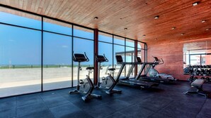 Un gimnasio con equipo de ejercicio, amplias ventanas y vista al cielo.