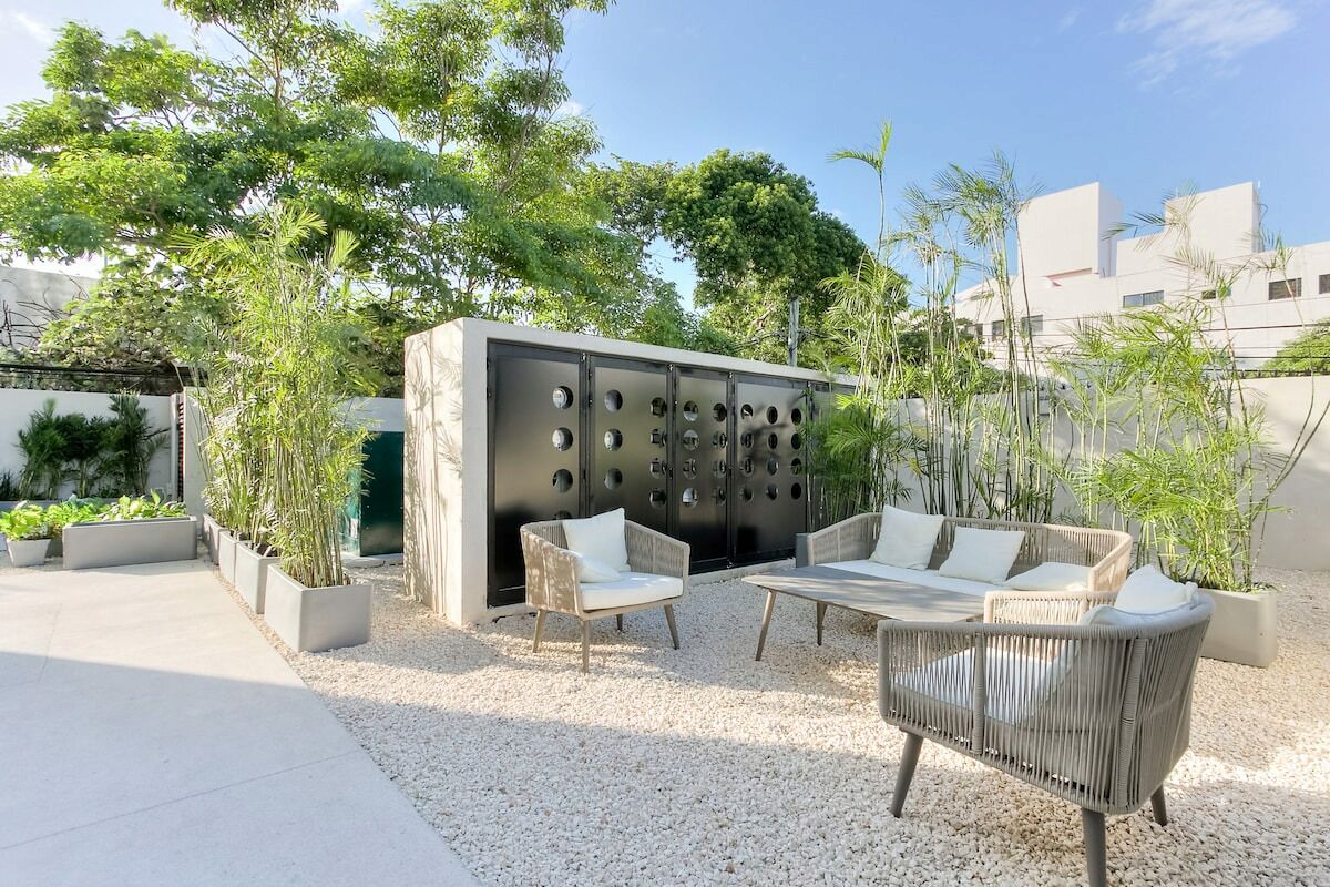 An outdoor seating area with a modern design, featuring a sofa and chairs, surrounded by planters and a decorative wall with circular cutouts.