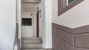 A hallway with a set of stairs leading to a door, a mailbox, and a security camera.
