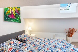 Ein Schlafzimmer mit Bett, Nachttisch, Lampe, Heizkörper, Fenster und einem Bild an der Wand.