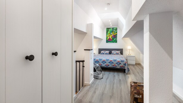 A bedroom with a bed, a nightstand, a lamp, and a painting on the wall.