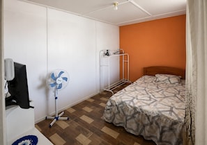 A bedroom with a bed, a standing fan, a TV, and a clothes drying rack.
