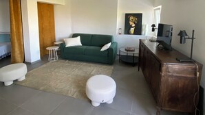 Een moderne woonkamer met een groene bank, een witte poef, een klein rond tafeltje en een houten kast.