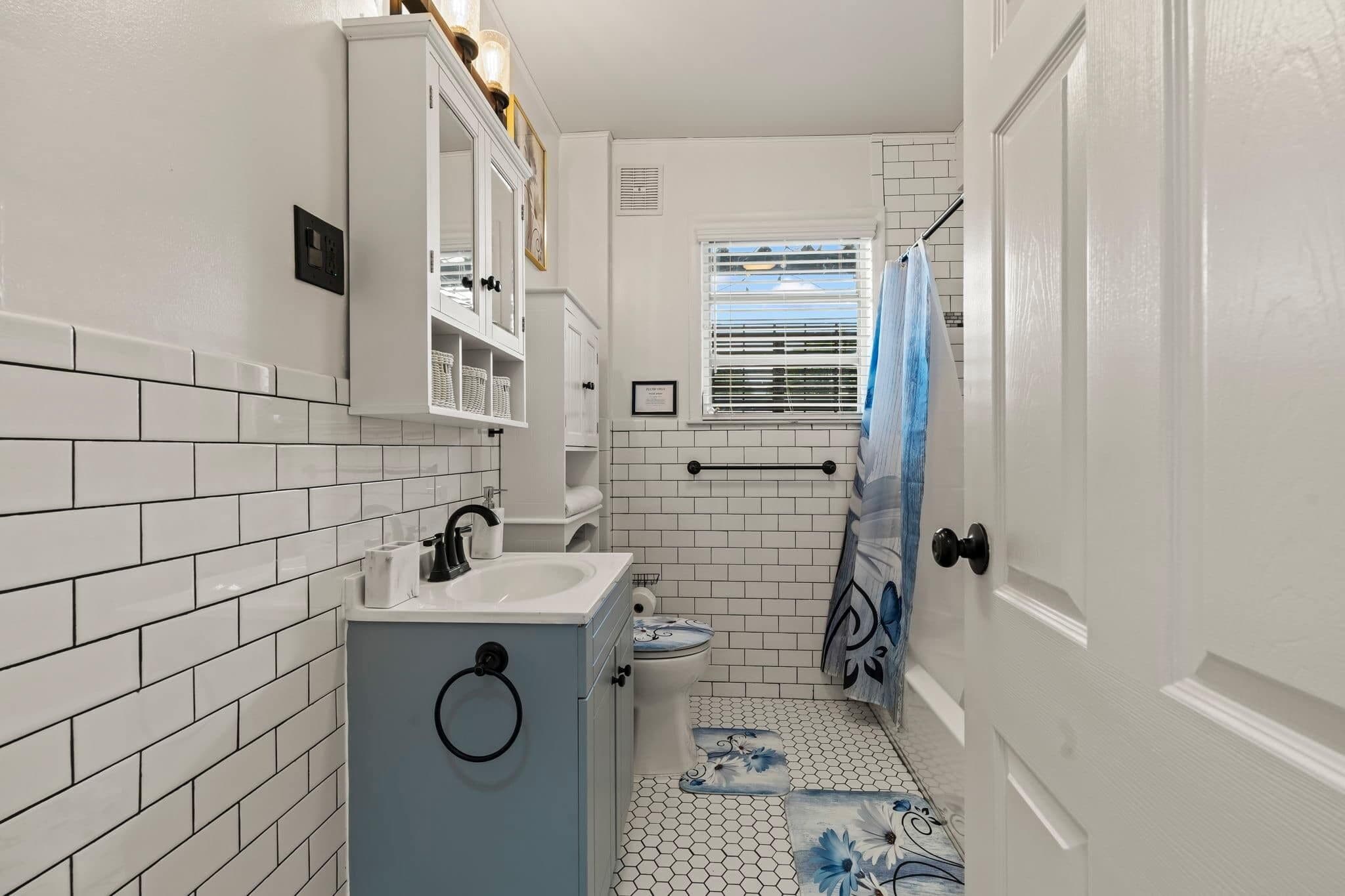 A bathroom with white tiled walls, a sink, a toilet, and a shower curtain.