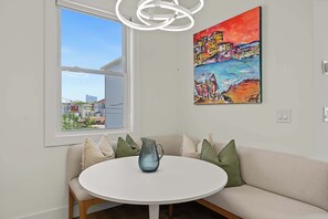 A room with a white round table, a beige sofa with cushions, a colorful painting on the wall, and a window with a view of buildings. - Casino Club House 1 block to Tropicana (Atlantic City)