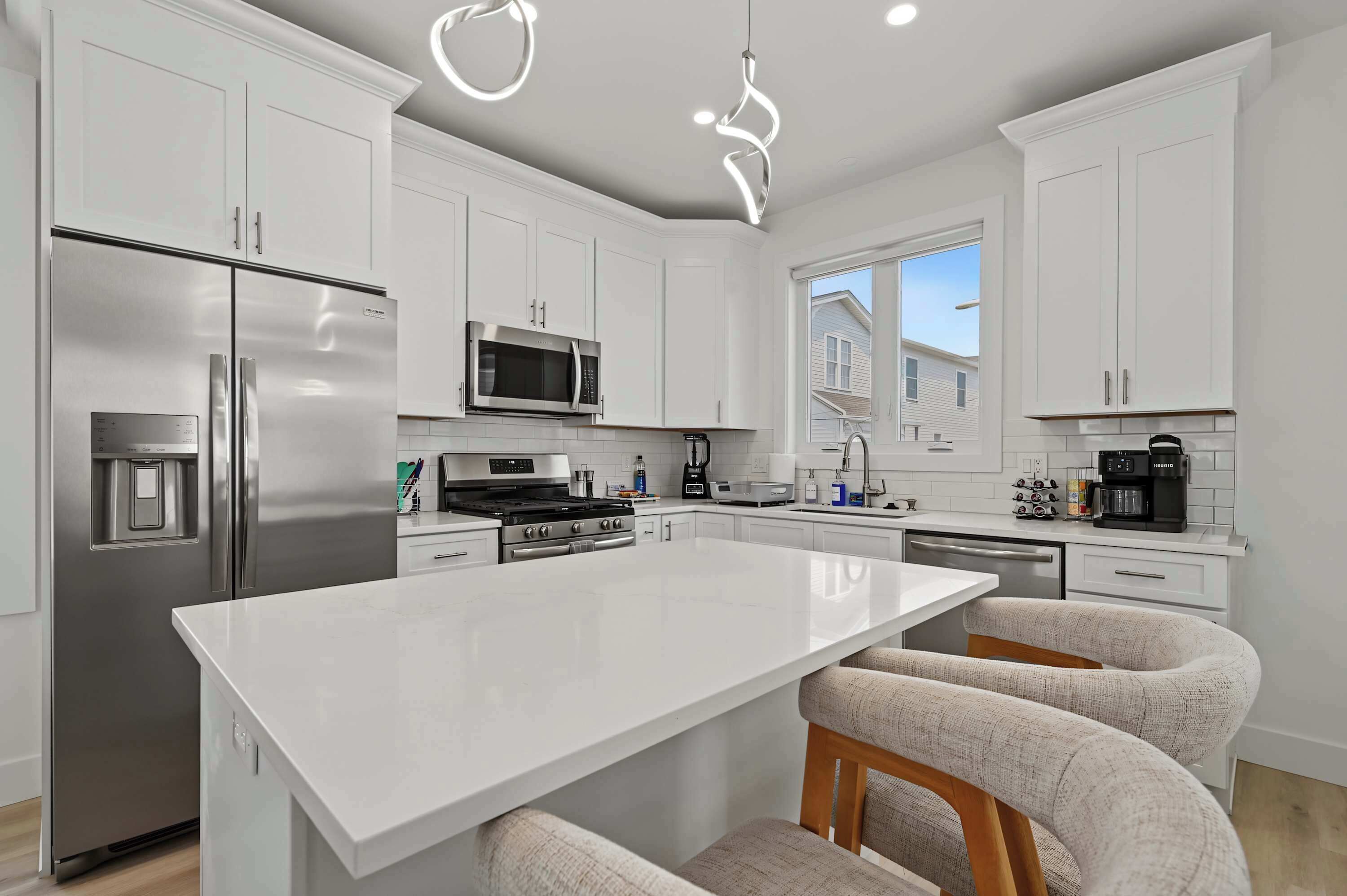 Una cocina moderna con armarios blancos, electrodomésticos de acero inoxidable y una isla central con taburetes de bar.