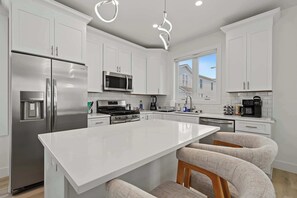 A modern kitchen with white cabinetry, stainless steel appliances, and a central island with bar stools. - Casino Club House 1 block to Tropicana (Atlantic City)