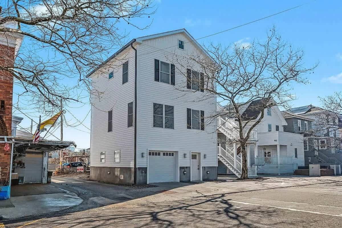A two-story white building with a garage, a small porch, and a staircase leading to the second floor.
