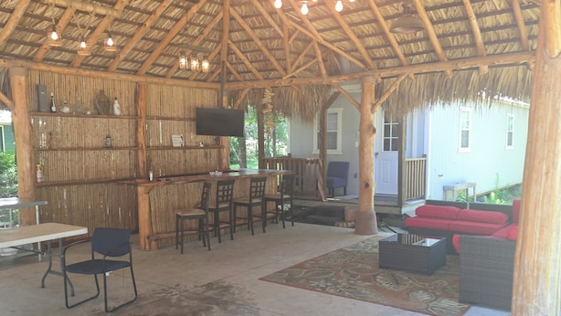 An outdoor covered area with a thatched roof, a bar with stools, and seating arrangements. - Cozy 1-bedroom cabin in serene Magnolia with AC (Magnolia)
