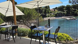 An outdoor seating area with tables and chairs, overlooking a body of water and a rocky shoreline. - In the heart of the Calanque du Cap Rousset—Apartment with a sea view, perfect for a romantic getaway! (Carry-le-Rouet)