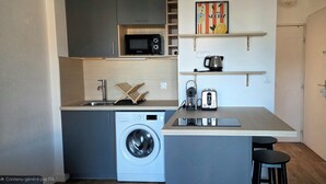 A compact kitchen with a washing machine, microwave, kettle, and a small dining area. - In the heart of the Calanque du Cap Rousset—Apartment with a sea view, perfect for a romantic getaway! (Carry-le-Rouet)