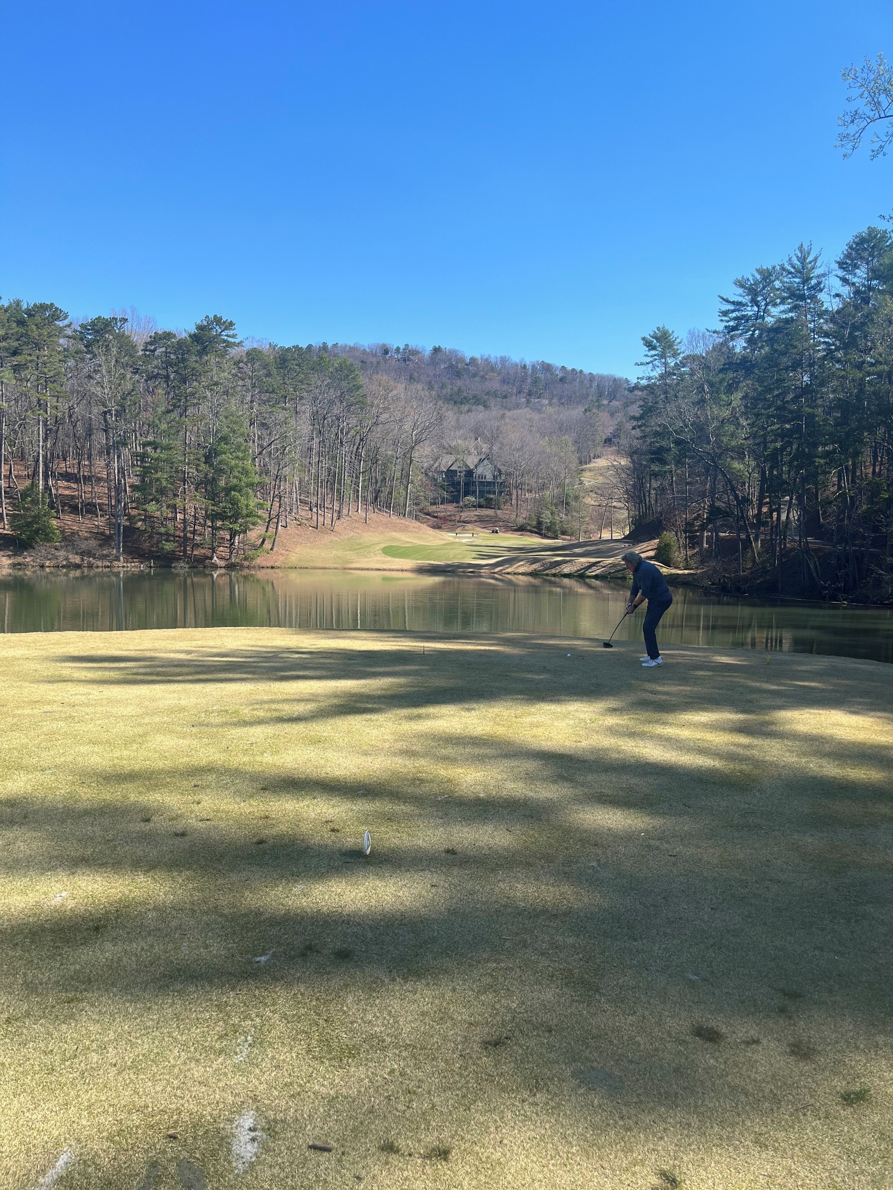 A golf course with a pond, trees, and a building in the background.