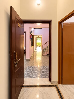 Un pasillo con una puerta de madera con el número '102' que da a una habitación con piso de baldosas y una escalera.