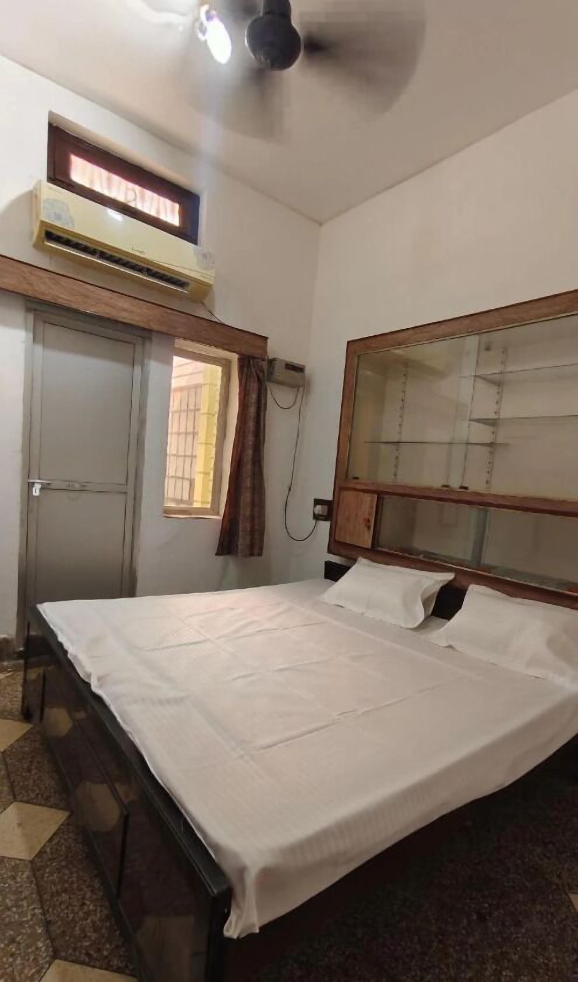 Un dormitorio con cama, ventilador de techo, unidad de aire acondicionado, ventana y puerta.