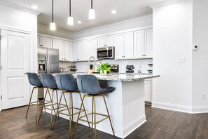 Una cocina moderna con armarios blancos, un refrigerador de acero inoxidable, un microondas y una barra con taburetes.