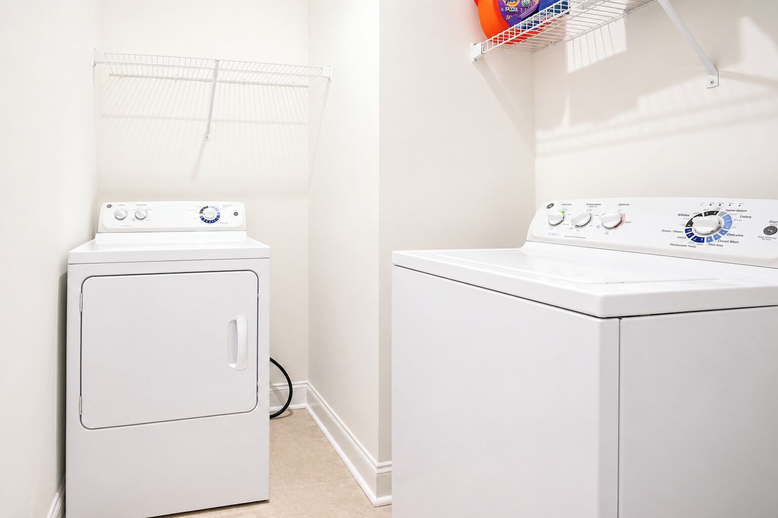 A laundry room with a front-loading washer and dryer, a drying rack, and a wall-mounted shelf with a basket.