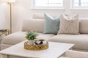 A living room with a sofa, decorative pillows, a small table with a plant and remote controls, and a floor lamp. - The Getaway, 2mi to SQ, +pool, Velvet Ditch Villas (Oxford)