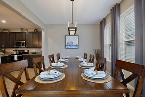 A dining room with a wooden table set for six, flanked by dark wooden chairs, a hanging light fixture, and a framed picture on the wall. - The Magic Haven - 5BR - Sleeps 13 - Near Disney (Davenport)